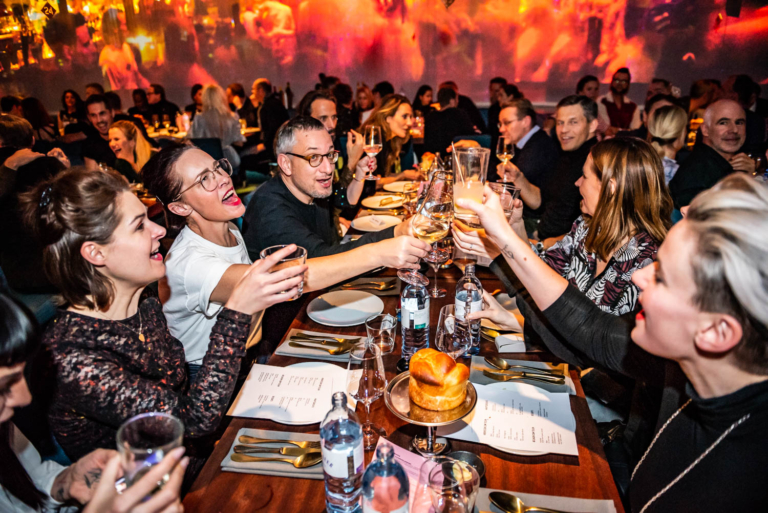 Guests raising their glasses at a long dinner table